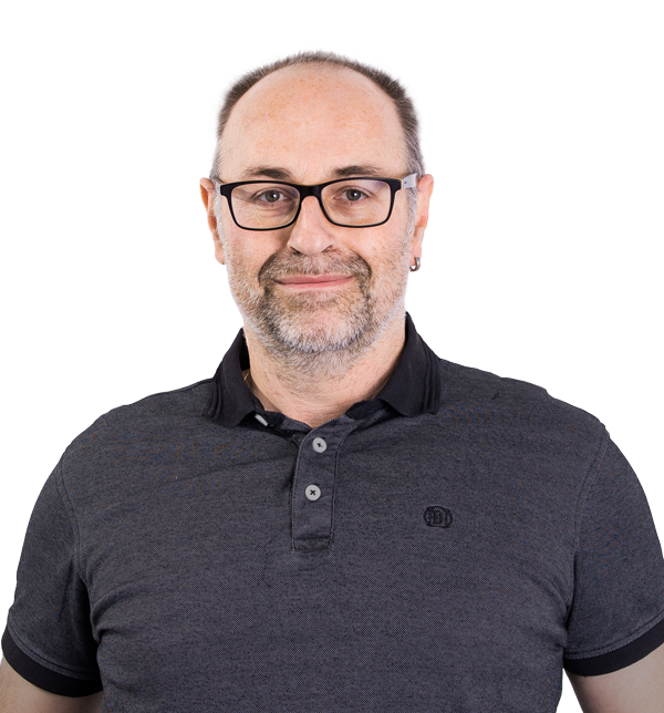 Ein Mann mittleren Alters mit Brille, kurzen grauen Haaren und einem Bart lächelt leicht. Er trägt ein dunkles Poloshirt und steht vor einem schlichten, hellen Hintergrund.