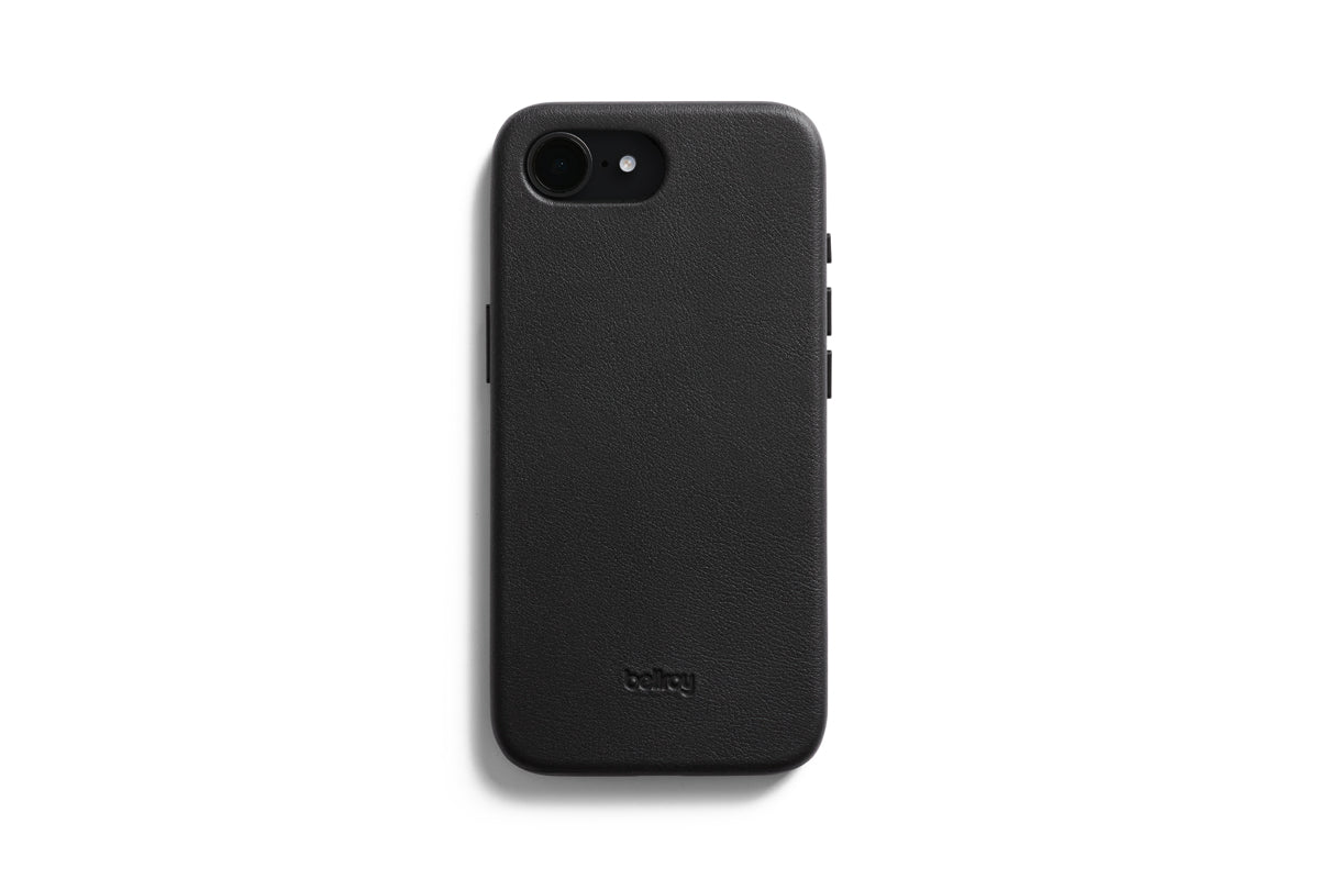 Eine Bellroy-Hülle – 0 Karten, iPhone 16e/17e – Schwarz umhüllt ein schwarzes Smartphone, das mit dem Display nach unten auf einem weißen Hintergrund liegt. Die strukturierte Hülle, die MagSafe-kompatibel ist und speziell für das iPhone 16e entwickelt wurde, trägt das Bellroy-Logo als Prägung im unteren Bereich.