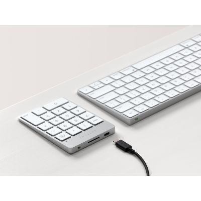 Ein „Satechi Slim Wireless Keypad Silver“ von Satechi fügt sich elegant in einen weißen Schreibtisch ein und dient als kabellose Zifferntastatur sowie als Tastaturerweiterung, wobei ein USB-C-Ladekabel praktischerweise direkt neben dem Ziffernblock angebracht ist.