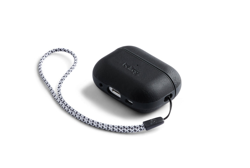 Eine Bellroy AirPods Jacket Pro (2. Generation) in Schwarz, die sich durch eine rechteckige Form mit einer strukturierten Oberfläche aus Premium-Leder und einem geflochtenen schwarz-weißen Handgelenkband auszeichnet, dargestellt vor einem weißen Hintergrund.