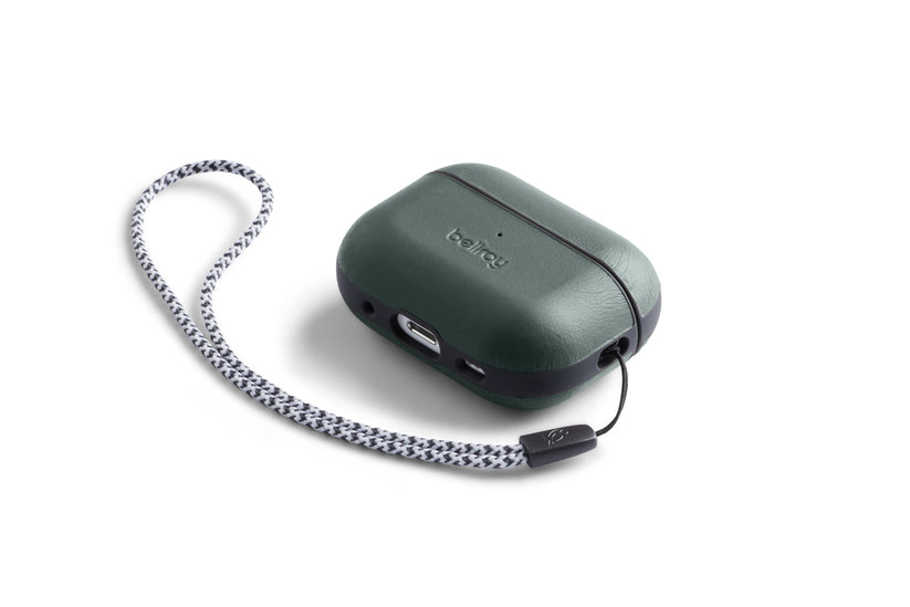 Eine dunkelgrüne (Everglade) „Bellroy AirPods Jacket Pro“ (2. Generation)-Hülle, die speziell für kabellose Ohrhörer entwickelt wurde und mit einem schwarzen Streifen versehen ist, wird mit einem geflochtenen weiß-schwarzen Handgelenkband geliefert. Diese aus hochwertigem Leder gefertigte Hülle verfügt über einen USB-C-Ladeanschluss und einen kleinen, gut sichtbaren Knopf.