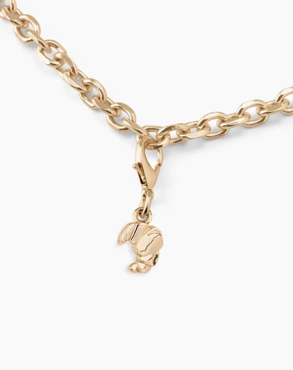Die „Ideal of Sweden Anhänger Croissant – Gold“, eine goldene Halskette mit einem croissantförmigen Anhänger und einem Karabinerverschluss, verkörpert die verspielte Eleganz, die für die Accessoires von Ideal of Sweden charakteristisch ist, und wird isoliert vor einem weißen Hintergrund gezeigt.