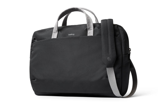 Wir stellen vor: die Bellroy Via Work Bag (Tech Briefcase) – Slate: Eine elegante schwarze Laptoptasche von Bellroy mit grauen Griffen und einem passenden, verstellbaren Schultergurt. Das minimalistische Design wird durch ein dezentes Bellroy-Logo oben in der Mitte abgerundet. Diese stilvolle Business-Tasche bietet ausreichend Platz für deinen Laptop und eignet sich ideal für den täglichen Gebrauch.