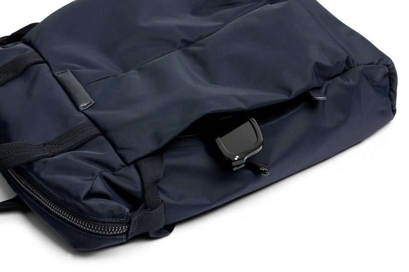 Eine Nahaufnahme des Bellroy Tokyo Totepack Compact in Marineblau zeigt das kompakte Design mit einer teilweise geöffneten Tasche, aus der eine schwarze Smartwatch hervorblitzt. Die wasserabweisende Stoffstruktur und der robuste Reißverschluss von Bellroy sind deutlich zu erkennen, während das praktische Laptopfach für zusätzliche Funktionalität sorgt.