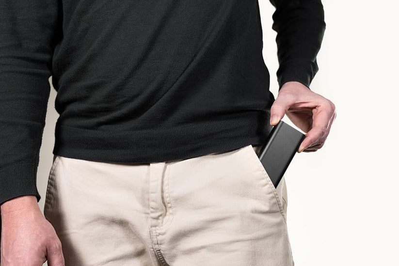 Siyah kazak ve bej pantolon giymiş bir kişi, mophie markalı dikdörtgen şekilli mophie Powerstation 10K - Schwarz cihazını ön cebine koyuyor.