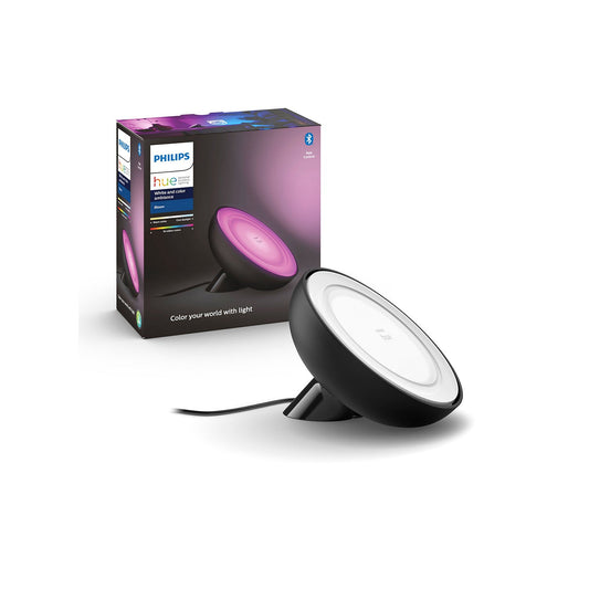 Eine Philips Hue Bloom Tischleuchte von Philips in Schwarz steht neben ihrer Verpackung. Die Lampe leuchtet mit farbigem Licht in Lila, der schwarze, runde Körper ist mit einem sichtbaren schwarzen Kabel angeschlossen.