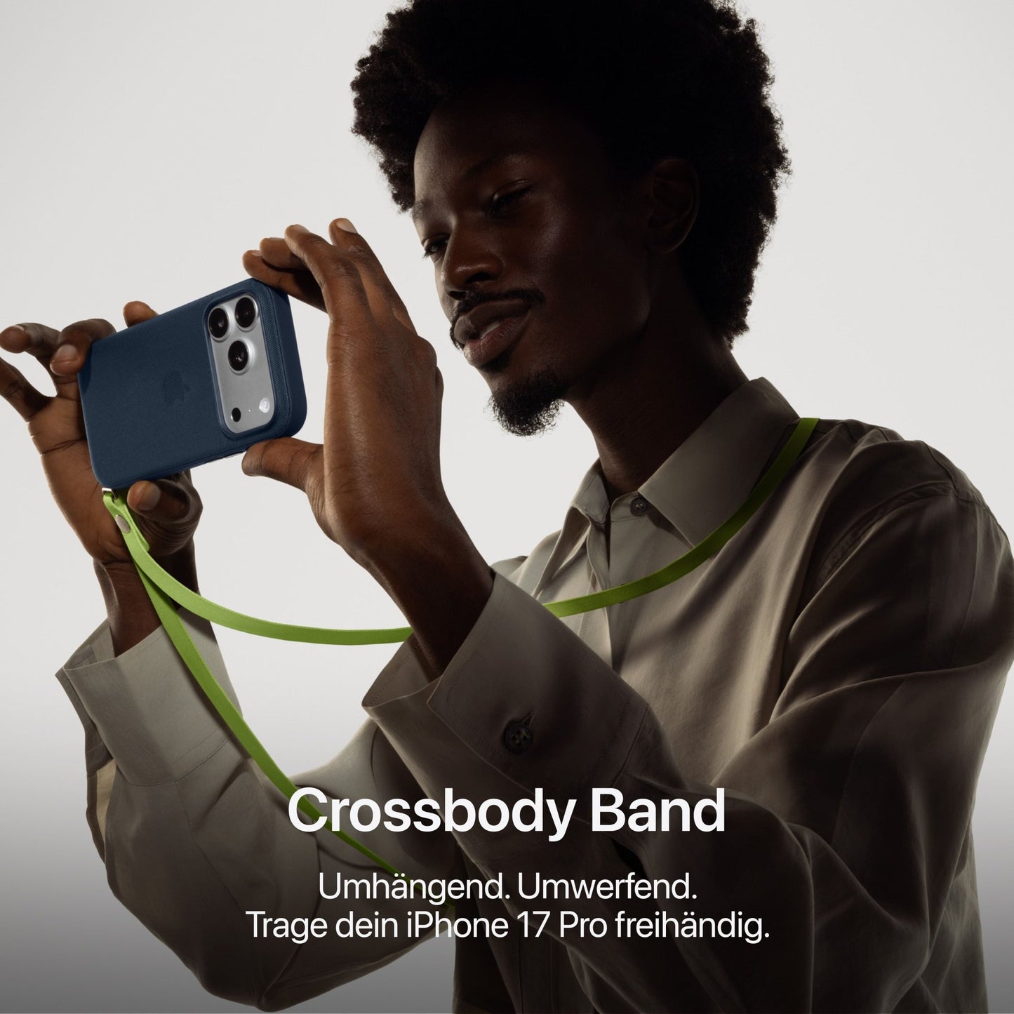A person holds an Apple iPhone 17 Pro 512GB in Cosmic Orange with a green crossbody band, wearing a beige shirt against a neutral background. German text highlights hands-free use and the powerful A19 Pro Chip.