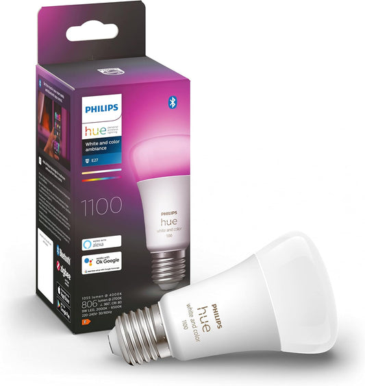 Ein Philips Hue White & Col. Amb. E27 Einzelpack 75W von Philips wird neben seiner Verpackung gezeigt, auf der Produktdetails und die Kompatibilität mit Alexa und Google Assistant hervorgehoben werden.