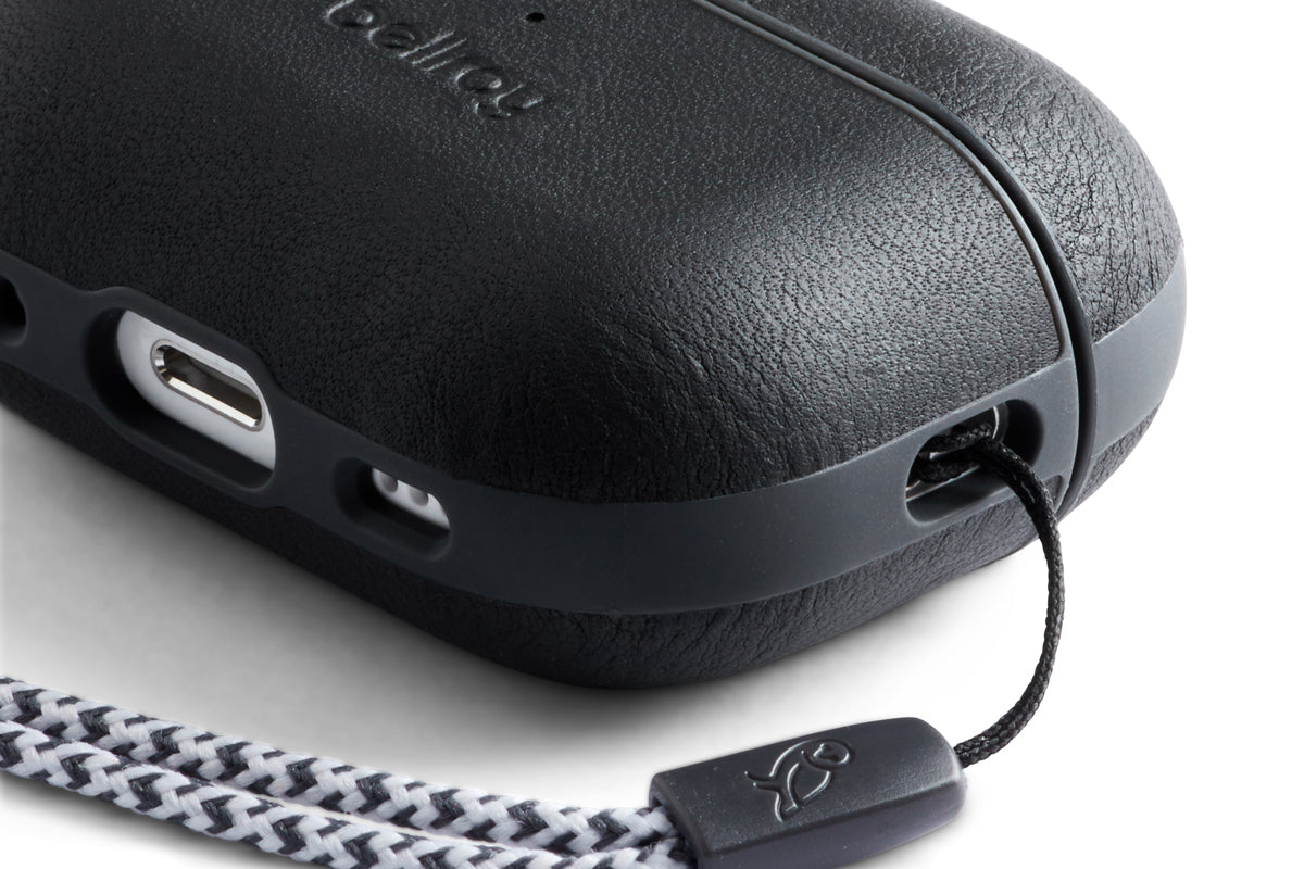 Nahaufnahme der Bellroy AirPods Jacket Pro (2. Generation) in Schwarz, die ihre strukturierte Premium-Leder-Oberfläche zeigt. Das maßgeschneiderte Etui verfügt über ein sichtbares Bellroy-Logo, einen USB-C-Ladeanschluss, eine durch die Ecke geführte Schlaufe sowie ein angebrachtes schwarz-weißes geflochtenes Band.