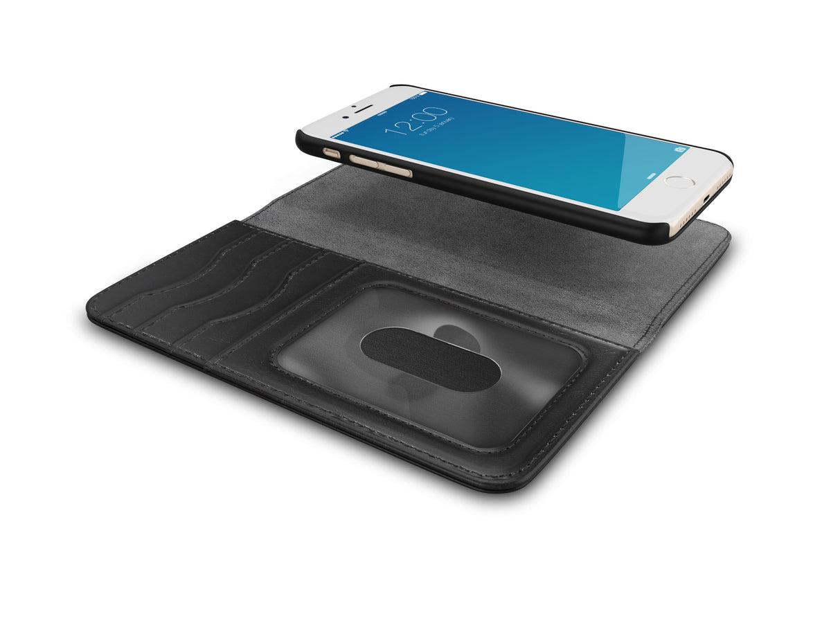 A black Magnet Wallet+ case from Ideal of Sweden is open, revealing card slots and a transparent ID window. Made from vegan materials, this case is designed for the iPhone 8 / 7 / 6 / 6S / SE. Above the case, a smartphone floats with its screen facing upward, showing the time as 12:00.