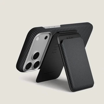 Eine gewebte Geldbörse Pitaka Magnetic Stand in Schwarz/Grau (Twill), die an der Rückseite eines Smartphones befestigt und in eine Ständerposition geklappt ist.