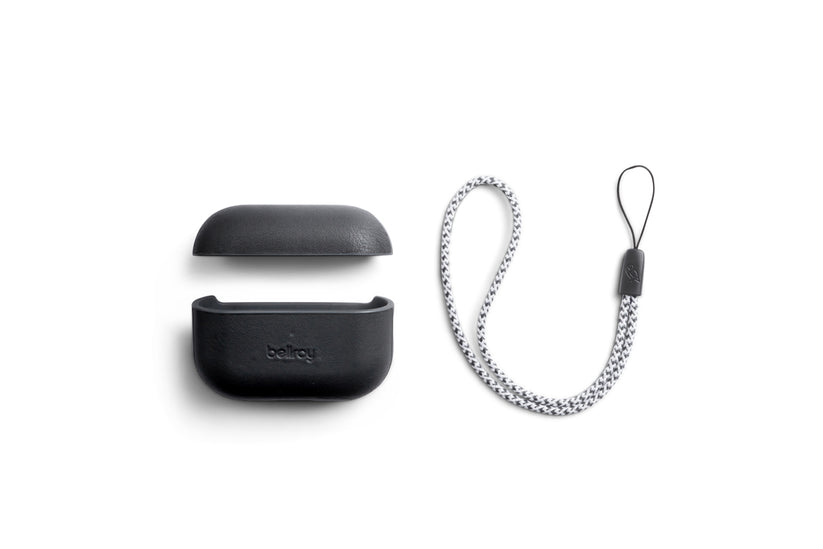 Die Bellroy AirPods Jacket Pro (2. Generation) in Schwarz, die auf eine perfekte Passform zugeschnitten ist, wird aufgeklappt neben einem geflochtenen grau-weißen Trageband mit schwarzer Befestigungsschlaufe vor einem weißen Hintergrund gezeigt.
