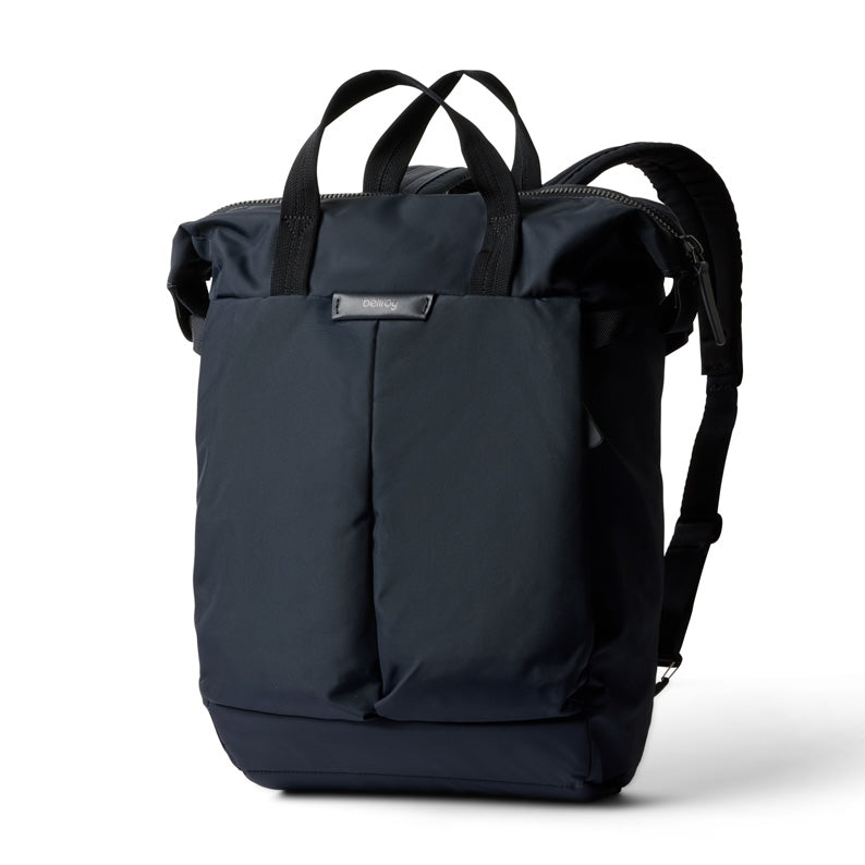 Ein marineblauer, wasserabweisender Bellroy Tokyo Totepack Compact ist vor einem weißen Hintergrund abgebildet. Dieser kompakte Rucksack verfügt über Tragegriffe an der Oberseite, Schulterriemen, ein schlankes, modernes Design mit einer Fronttasche, ein spezielles Laptopfach und ein kleines Bellroy-Markenetikett aus Metall.