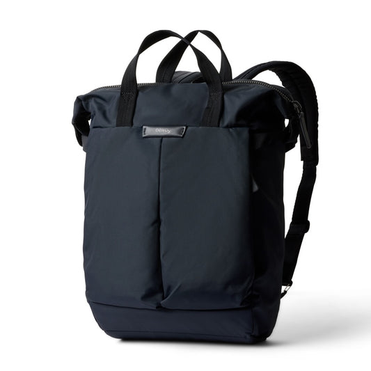Ein marineblauer, wasserabweisender Bellroy Tokyo Totepack Compact ist vor einem weißen Hintergrund abgebildet. Dieser kompakte Rucksack verfügt über Tragegriffe an der Oberseite, Schulterriemen, ein schlankes, modernes Design mit einer Fronttasche, ein spezielles Laptopfach und ein kleines Bellroy-Markenetikett aus Metall.