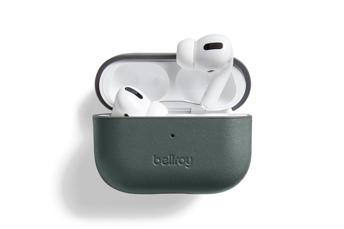 Ein Paar weiße kabellose Ohrhörer in einer offenen, dunkelgrünen „Bellroy AirPods Jacket Pro (2. Generation) – Everglade“-Hülle aus hochwertigem Leder, präsentiert vor weißem Hintergrund, um die passgenaue Form und die praktische USB-C-Ladefunktion zu verdeutlichen.