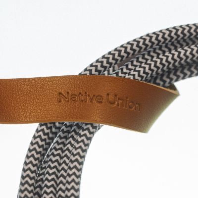 Ein 3 m langes Native Union Belt Cable XL (USB-C auf USB-C) in der Farbvariante „Zebra“ besticht durch ein geflochtenes schwarz-weißes Design, das durch einen braunen Lederriemen mit eingeprägtem Native Union-Logo geführt ist und so Stil und Funktionalität für den täglichen Gebrauch vereint.