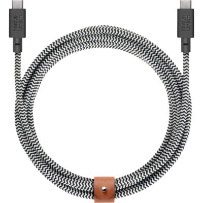 Ein Native Union Belt Cable XL USB-C auf USB-C, 3 m, Zebra, mit schwarz-weißem Flechtdesign, ist zu einer Schleife gewickelt und mit einem braunen Lederband gesichert. An den Enden sind beide Stecker sichtbar.
