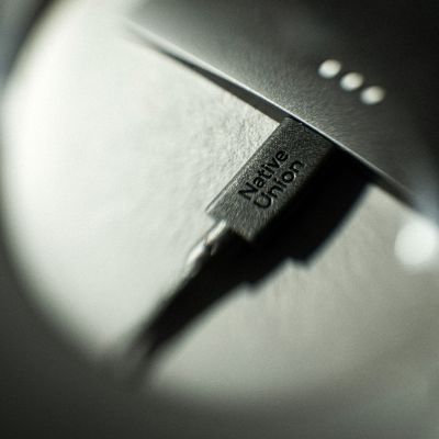 Nahaufnahme eines Native Union Belt Cable XL USB-C-zu-USB-C-Kabels (3 m) in der Farbe „Cosmos“, auf dem das „Native Union“-Logo zu sehen ist und das an ein Gerät angeschlossen ist. Der leicht unscharfe Soft-Focus-Effekt unterstreicht die Premium-Qualität dieses 3 Meter langen Ladekabels.