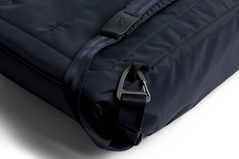 Nahaufnahme des Bellroy Tokyo Totepack Compact in Navy, die die Ecke der Tasche mit einem schwarzen Riemen, einer Metallschnalle und aufwendigen Nähten zeigt – und damit das kompakte Rucksack-Design von Bellroy aus wasserabweisendem Material unterstreicht.