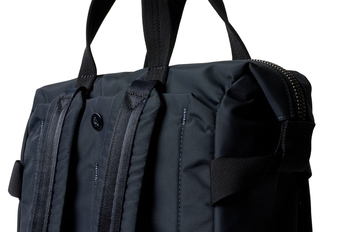 Eine Nahaufnahme des Bellroy Tokyo Totepack Compact in Marineblau mit robusten Tragegriffen, Rucksackträgern und einem gut sichtbaren Reißverschluss. Das wasserabweisende Material und das spezielle Laptopfach machen ihn sowohl praktisch als auch stilvoll – hier auf weißem Hintergrund abgebildet.